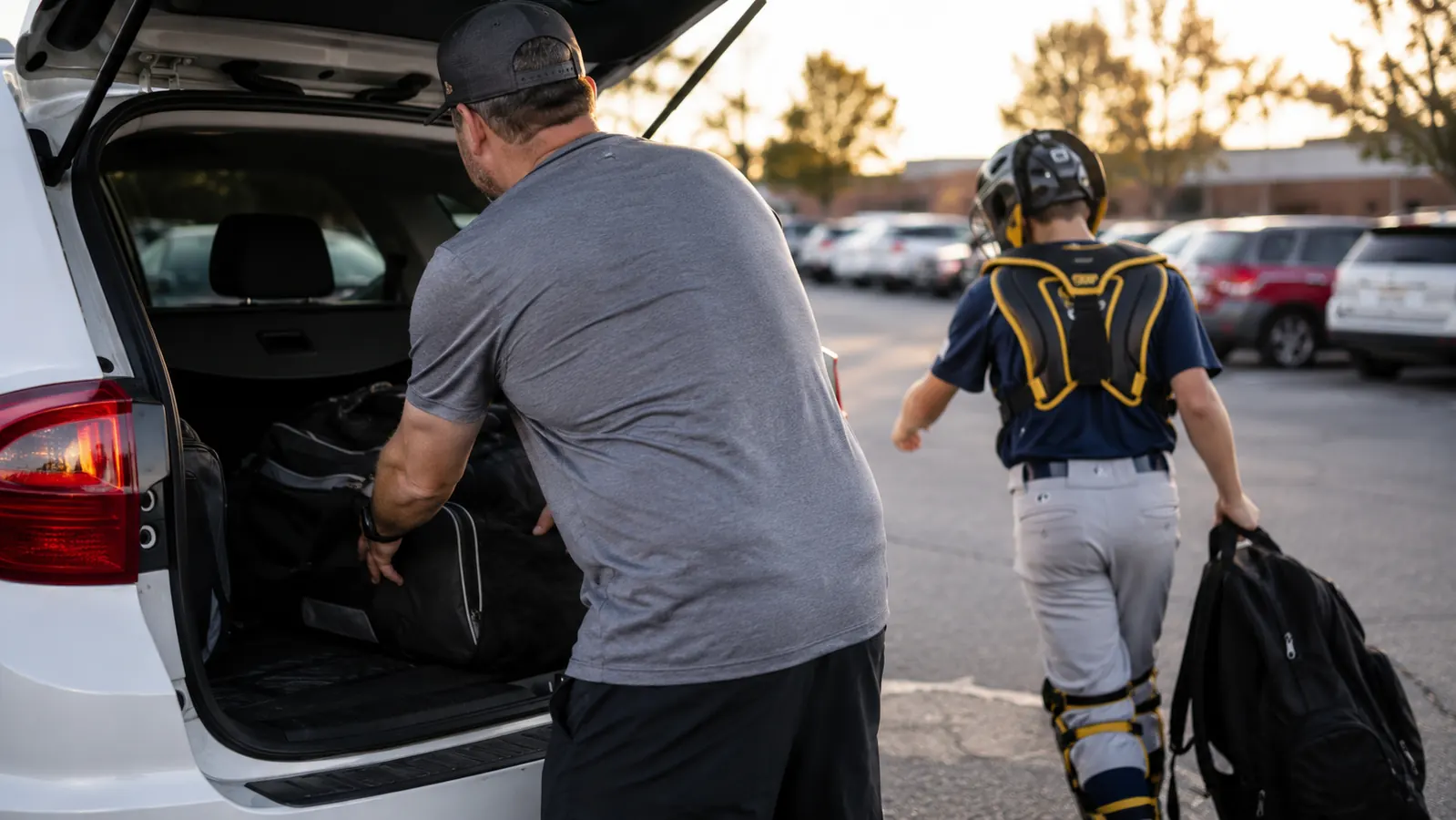 Dad and teenage son loading bat bags into the back of a car after practice