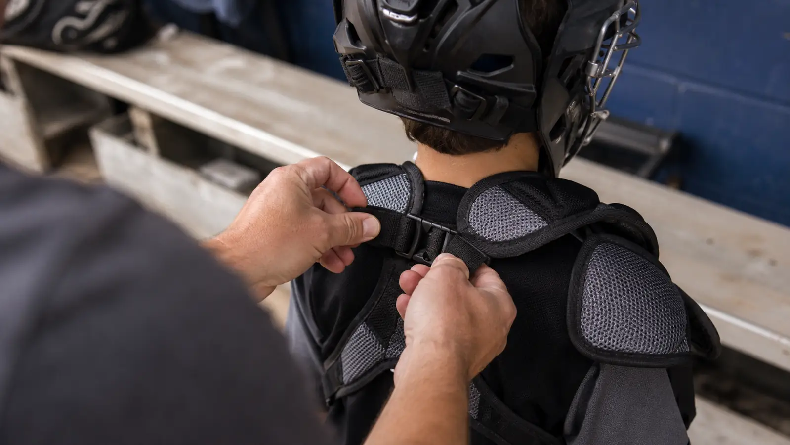 Parent adjusting the shoulder harness straps on a catcher's chest protector before a game