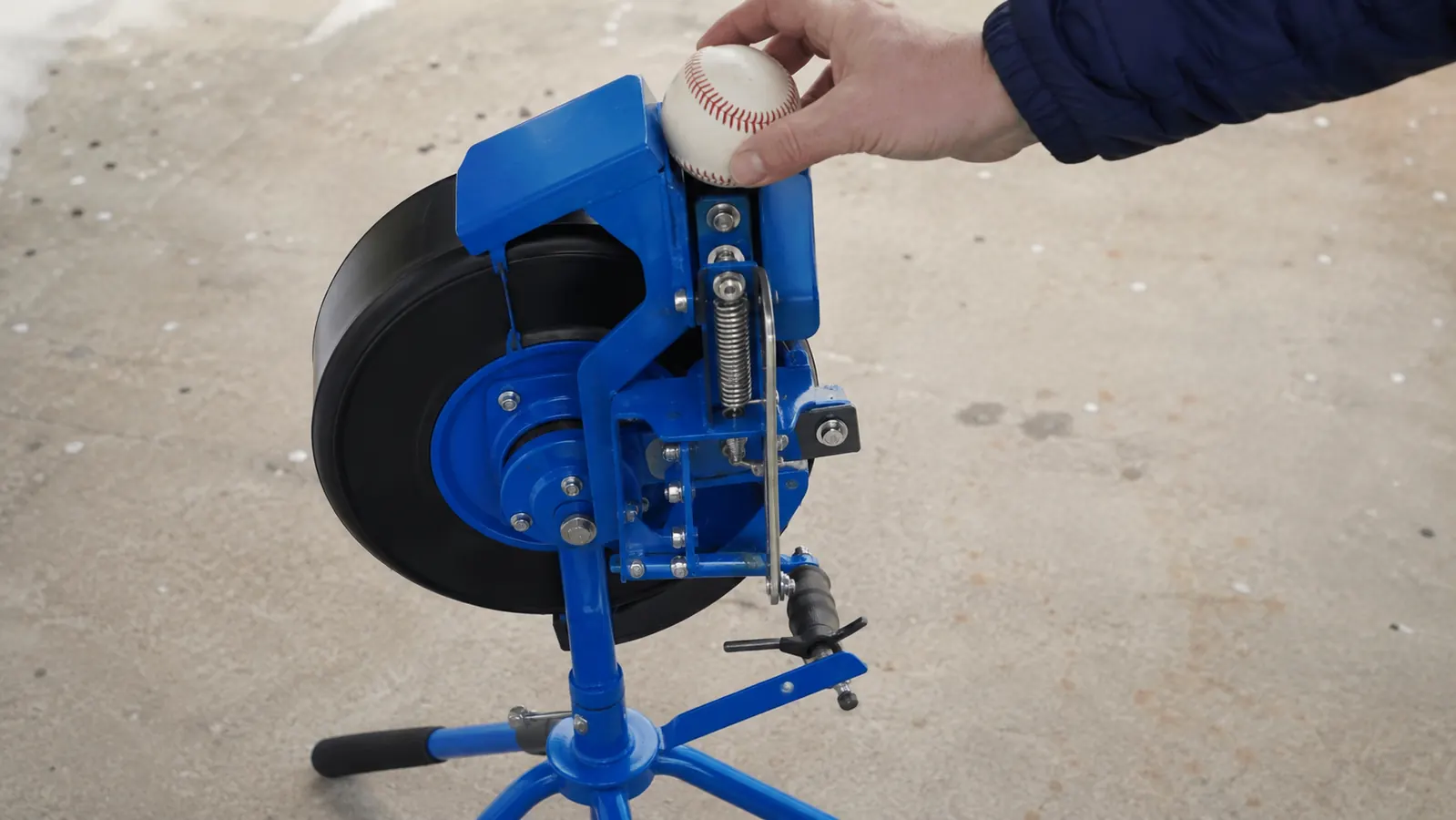 Hand loading a softball into the feed wheel of a portable pitching machine on a driveway