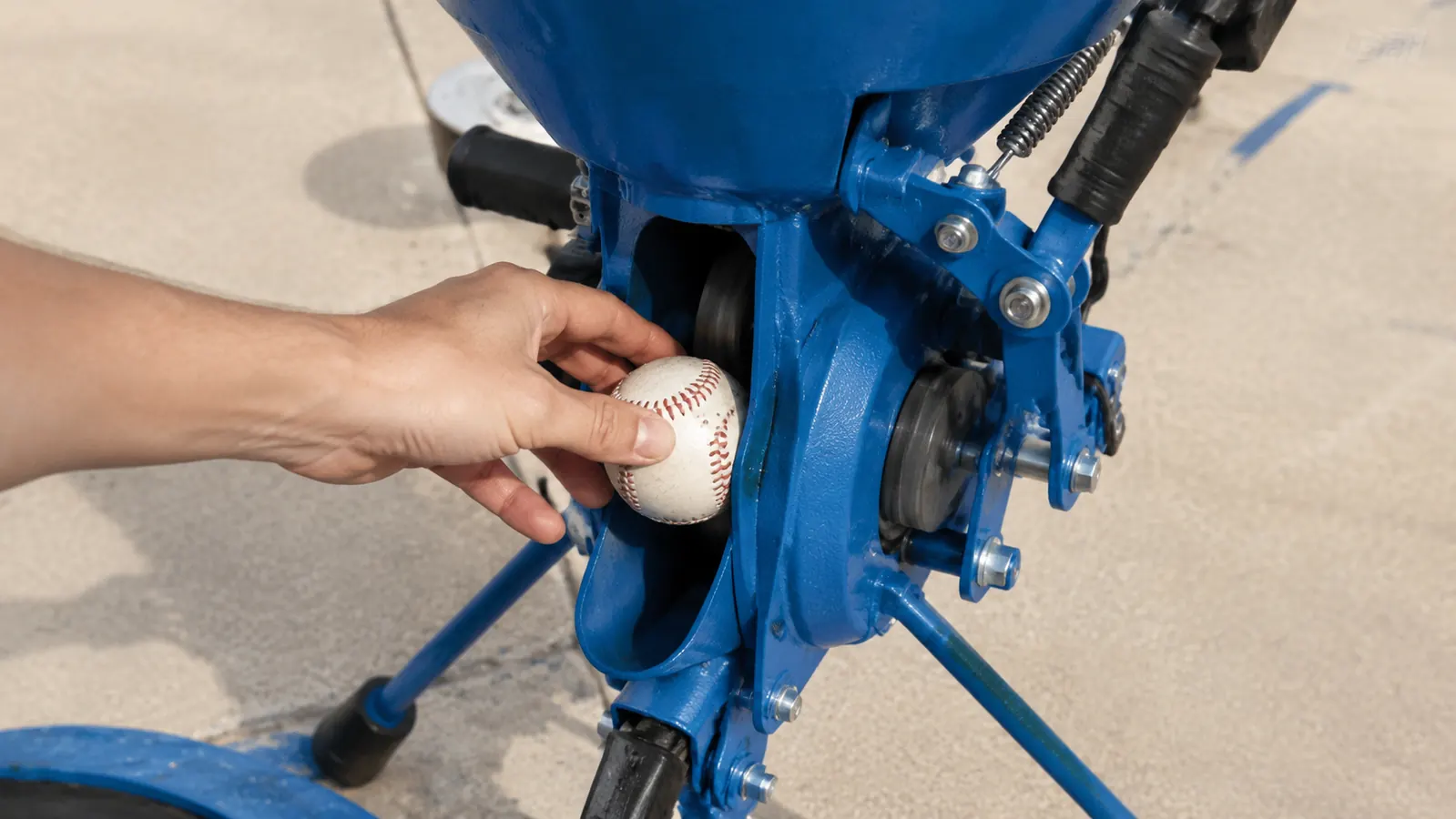 Close-up of a hand feeding a baseball into the spinning wheel of a Louisville Slugger Blue Flame pitching machine