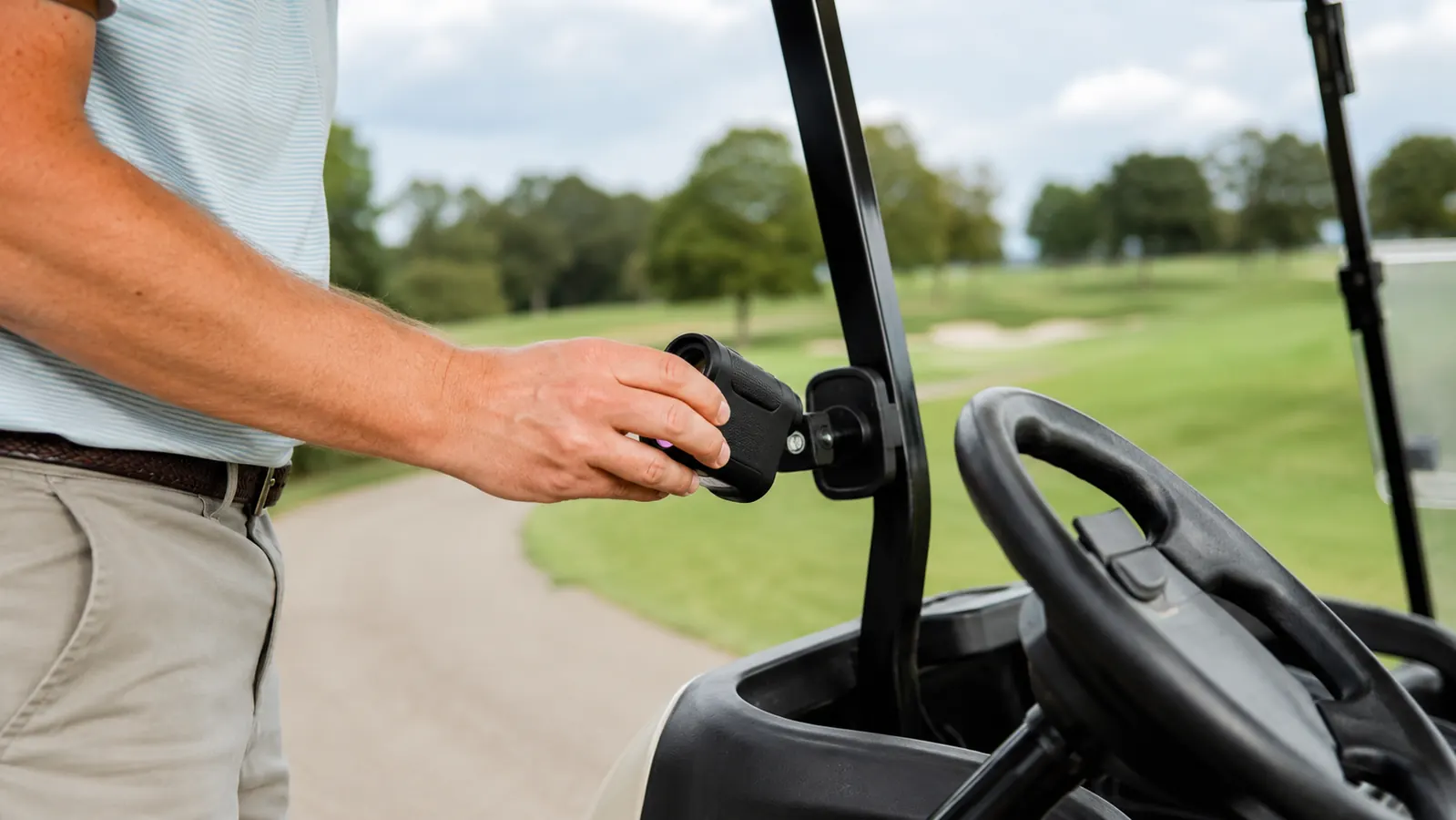 Golfer clipping a rangefinder to a magnetic cart bar mount before teeing off