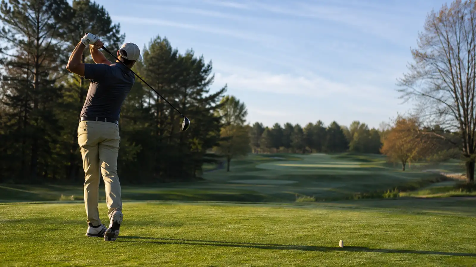 A golfer driving off the first tee on a spring morning at a public golf course