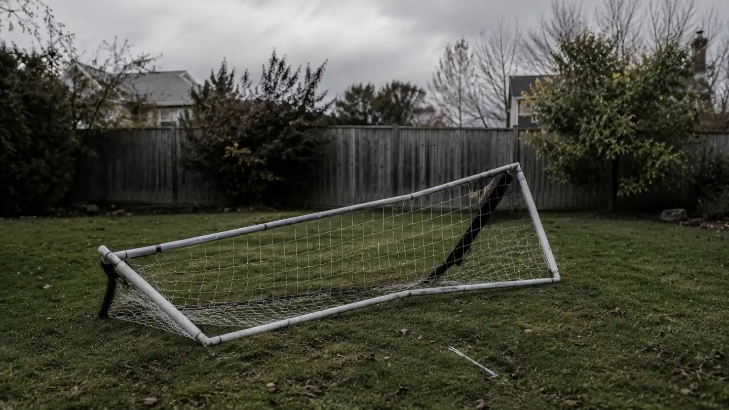 GoSports net frame tipped over sideways in a backyard after a gust of wind, poles still connected but base pulled loose