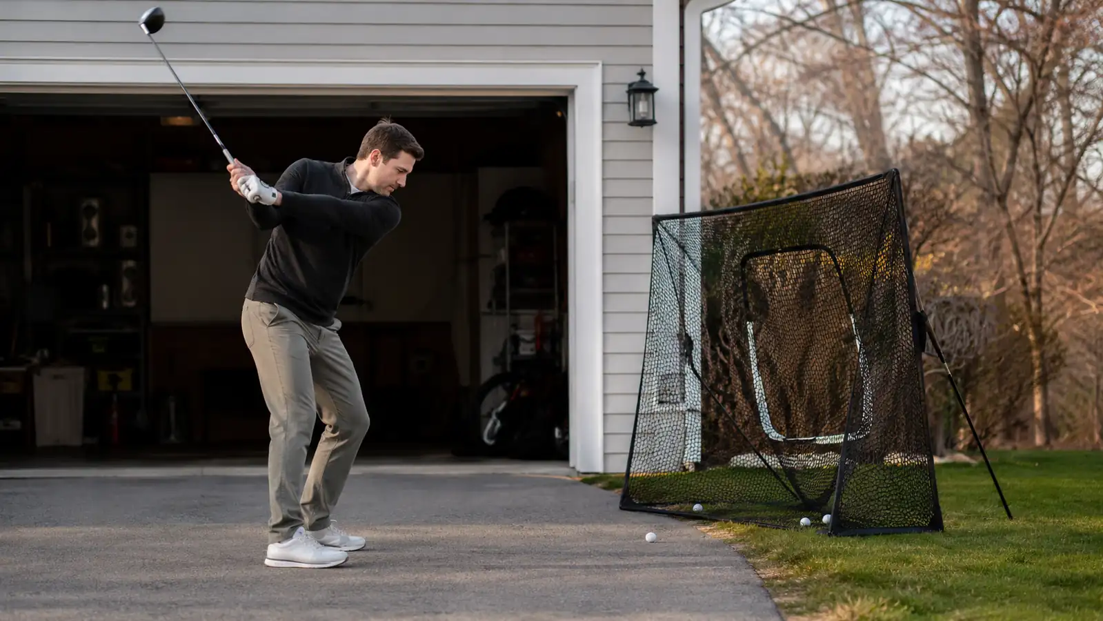 Golfer hitting a driver into the GoSports net set up on a driveway in early spring sunlight
