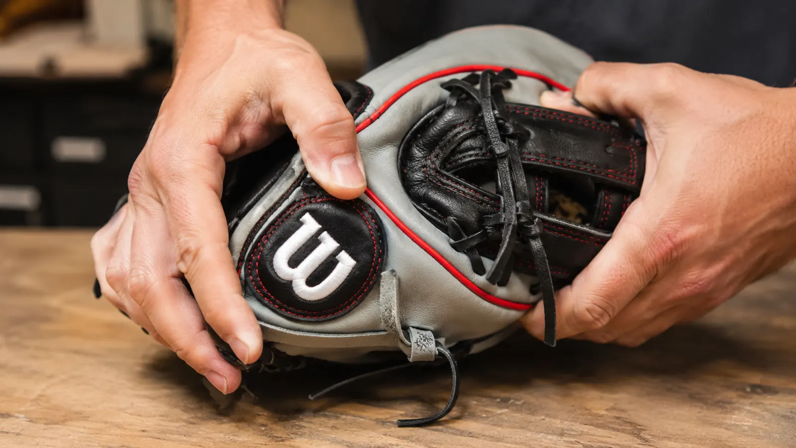 A pair of hands working the pocket of a dark brown leather infield glove, pressing the fingers closed around the palm