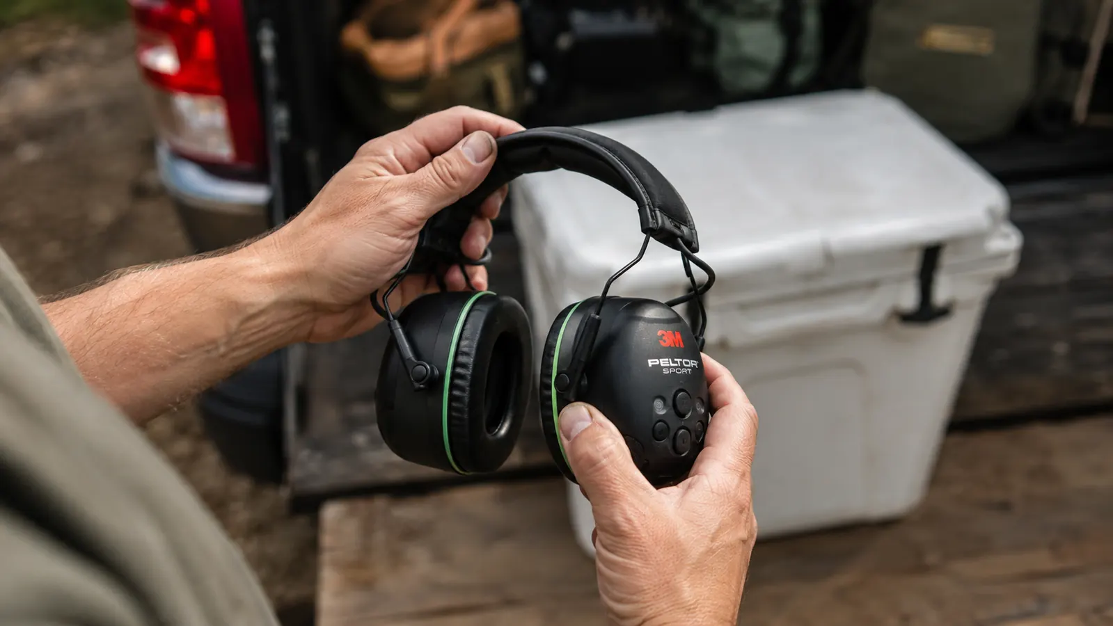 Hand adjusting the headband of black electronic earmuffs before putting them on