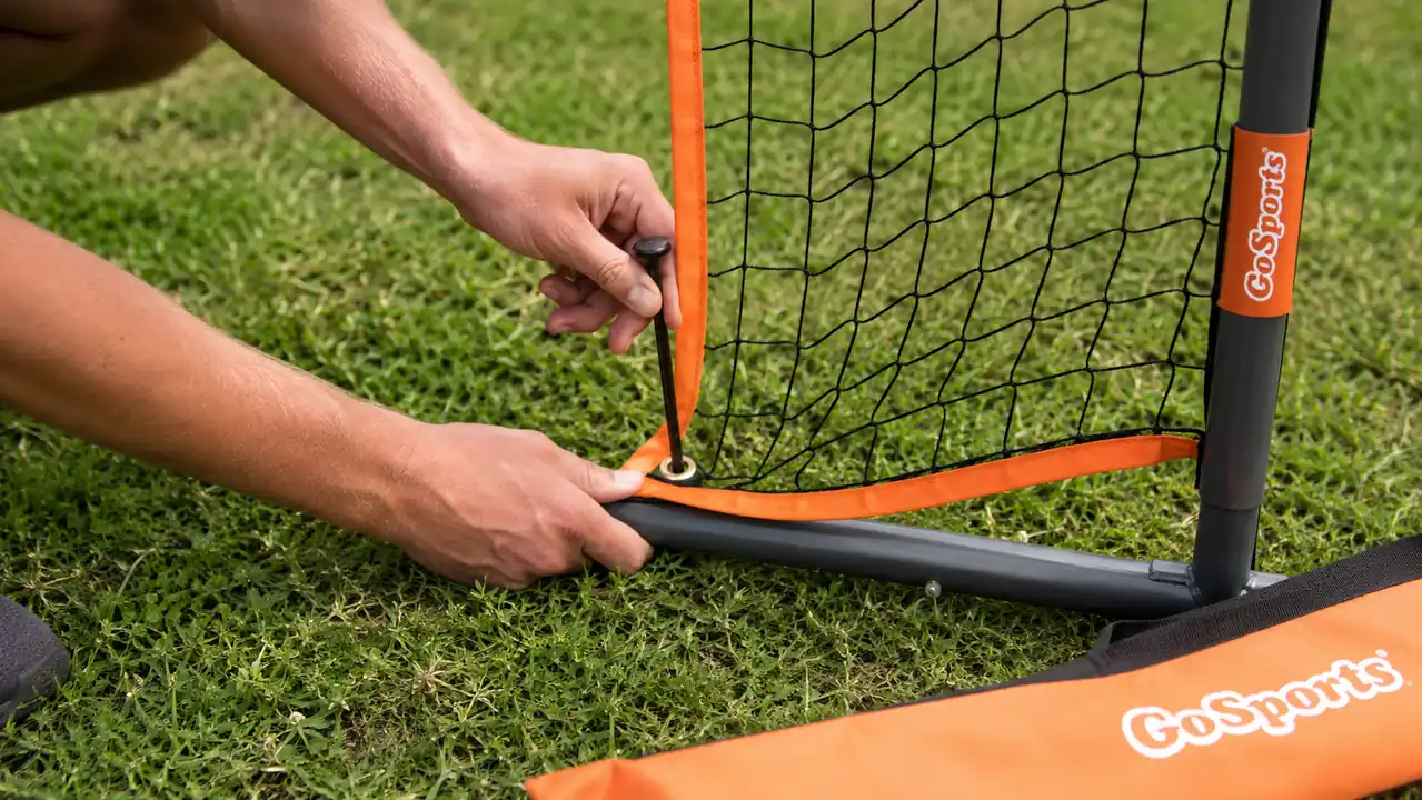 Hands staking a golf practice net into the ground at the corner of a backyard