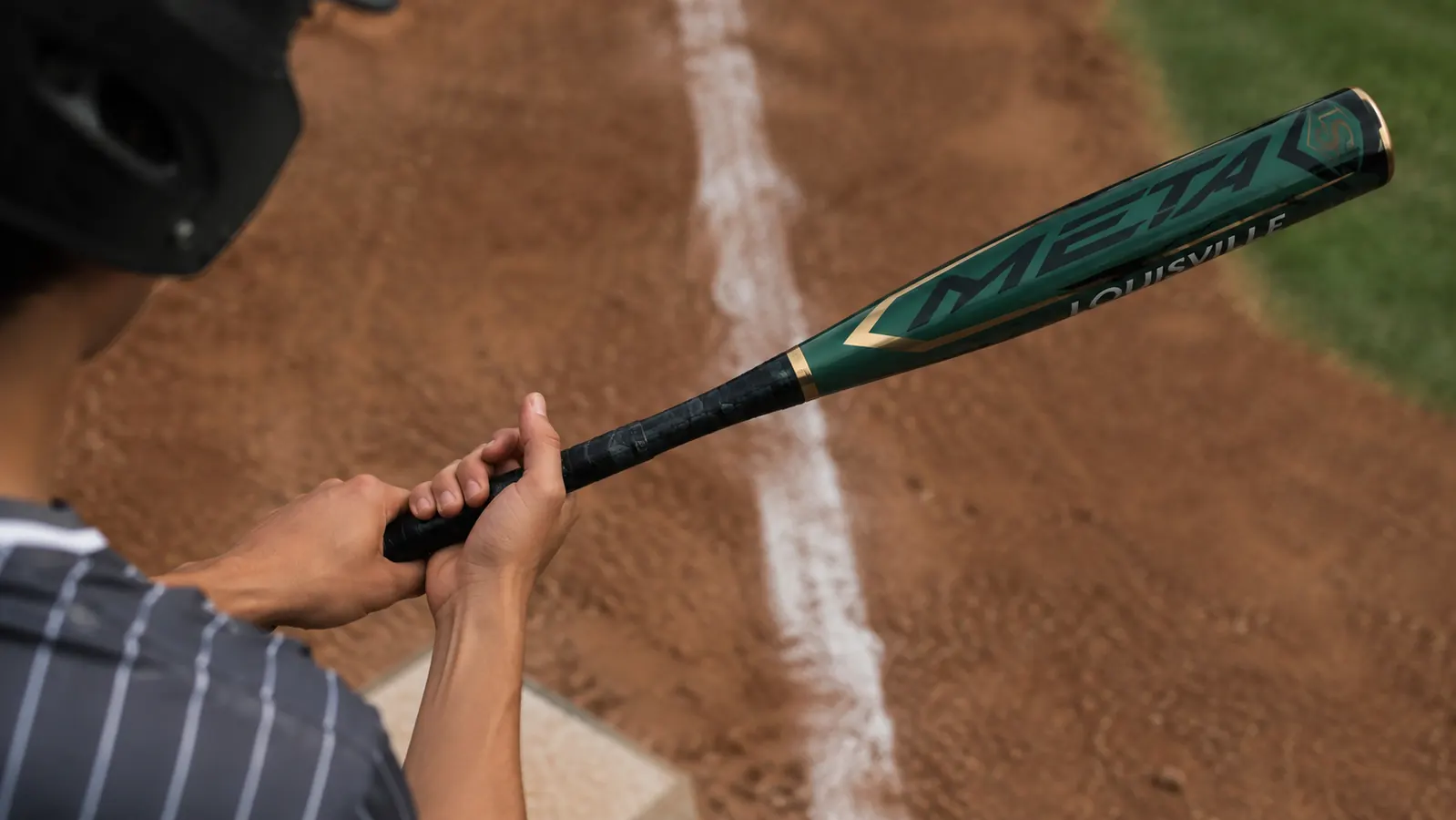 Close-up of hands gripping the handle of a Louisville Slugger Meta BBCOR bat near home plate