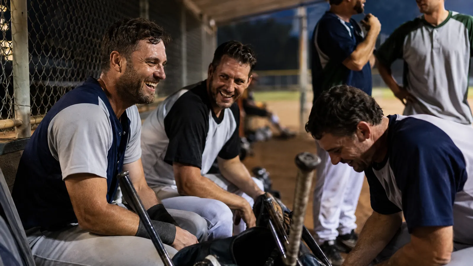Adult rec league player laughing with teammates in the dugout after a game