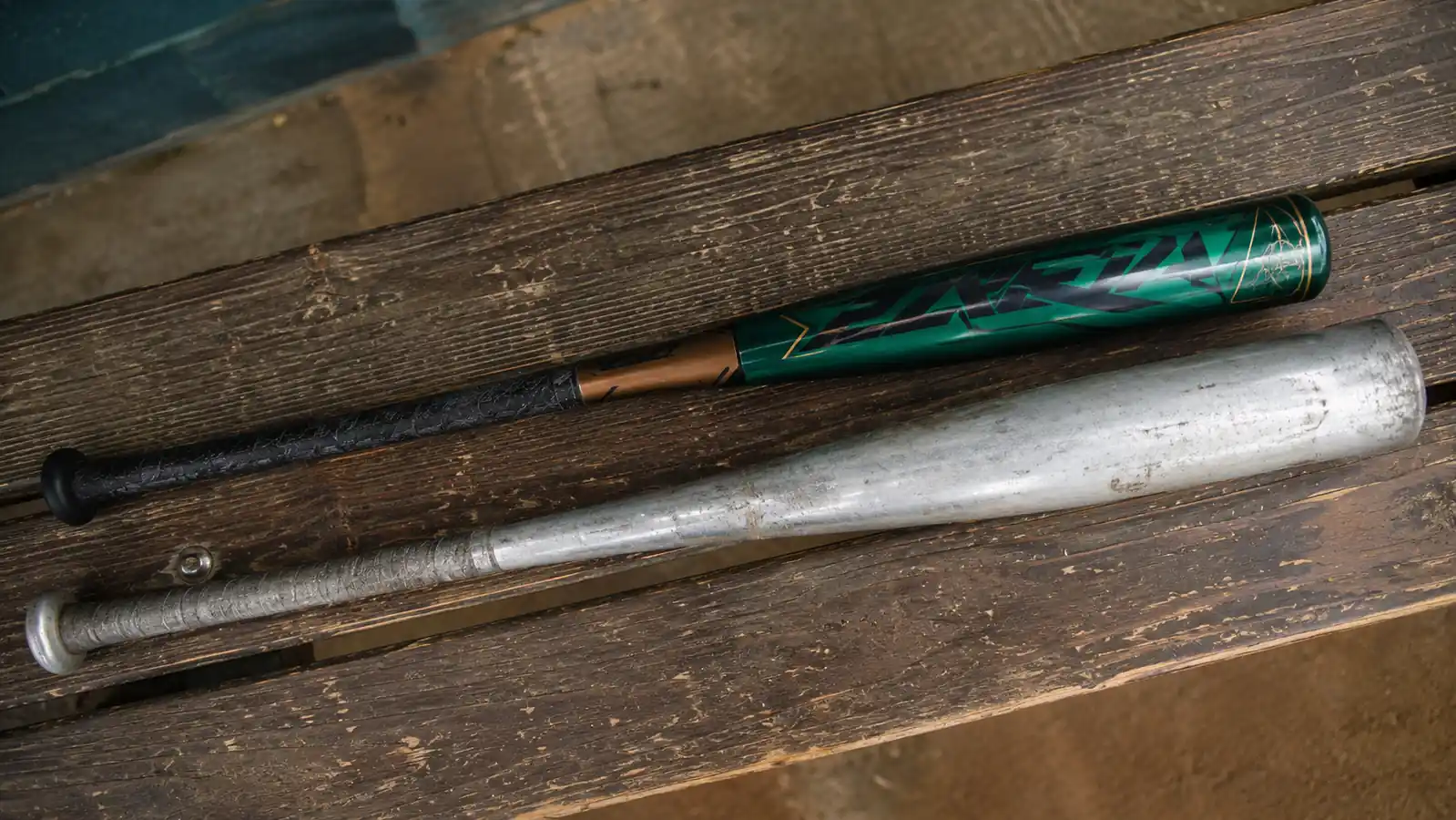 Two bats laid side by side on a bench, the Meta BBCOR and an older alloy bat, showing barrel size difference
