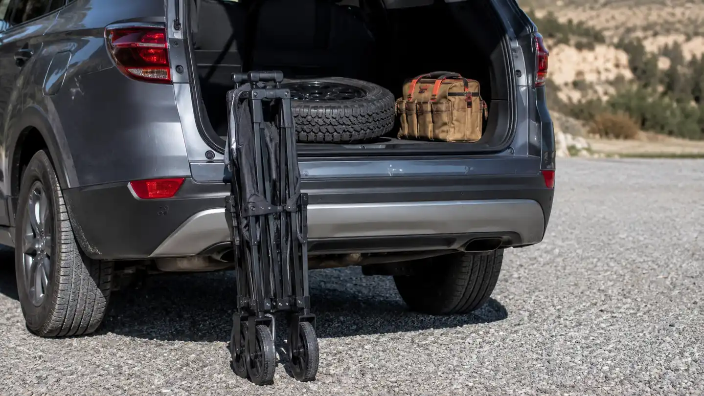 Folding wagon collapsed flat and leaning against the open trunk of a parked SUV