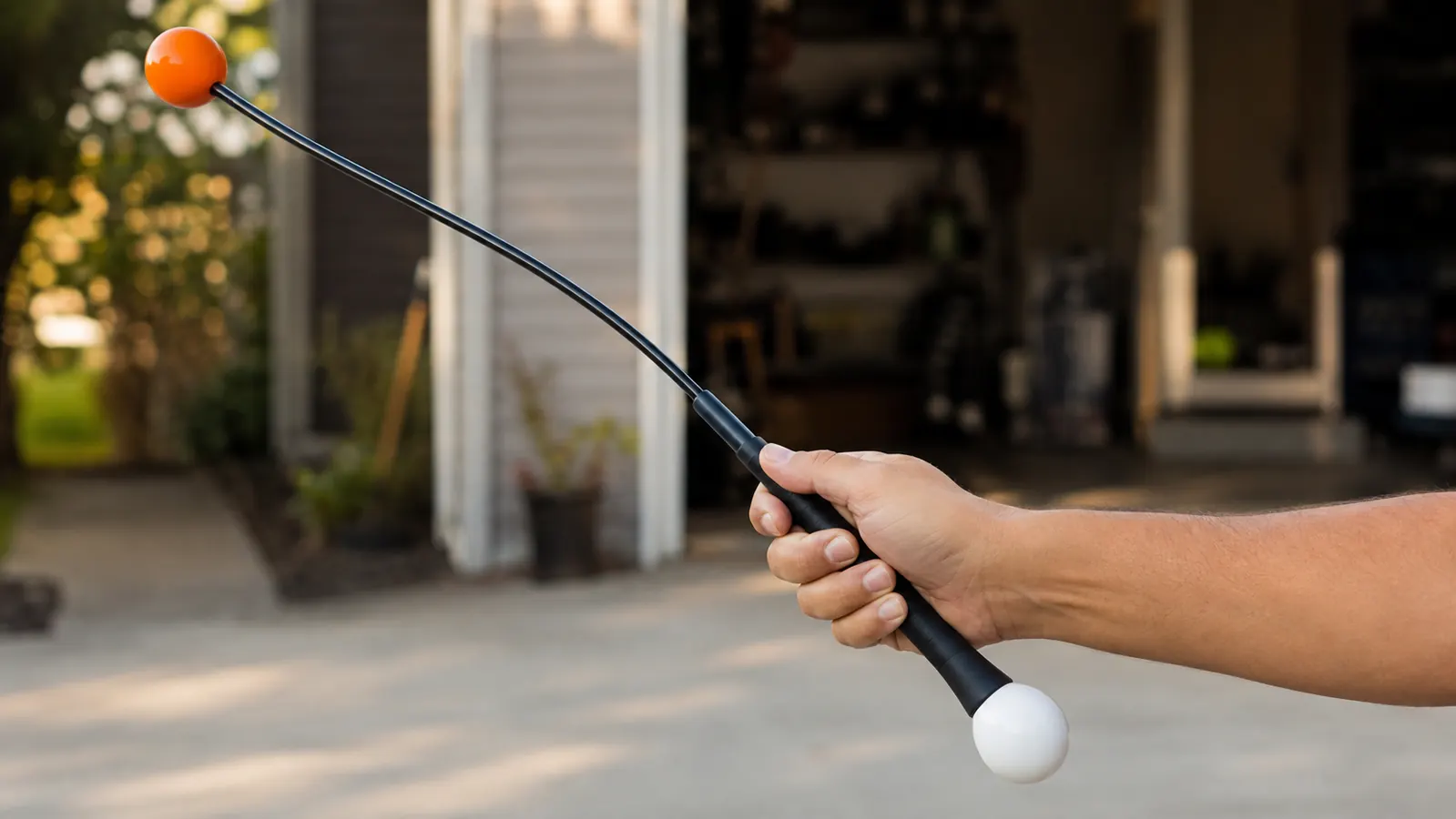 Hand gripping the Orange Whip trainer's handle with the flexible shaft and weighted orange ball visible mid-swing