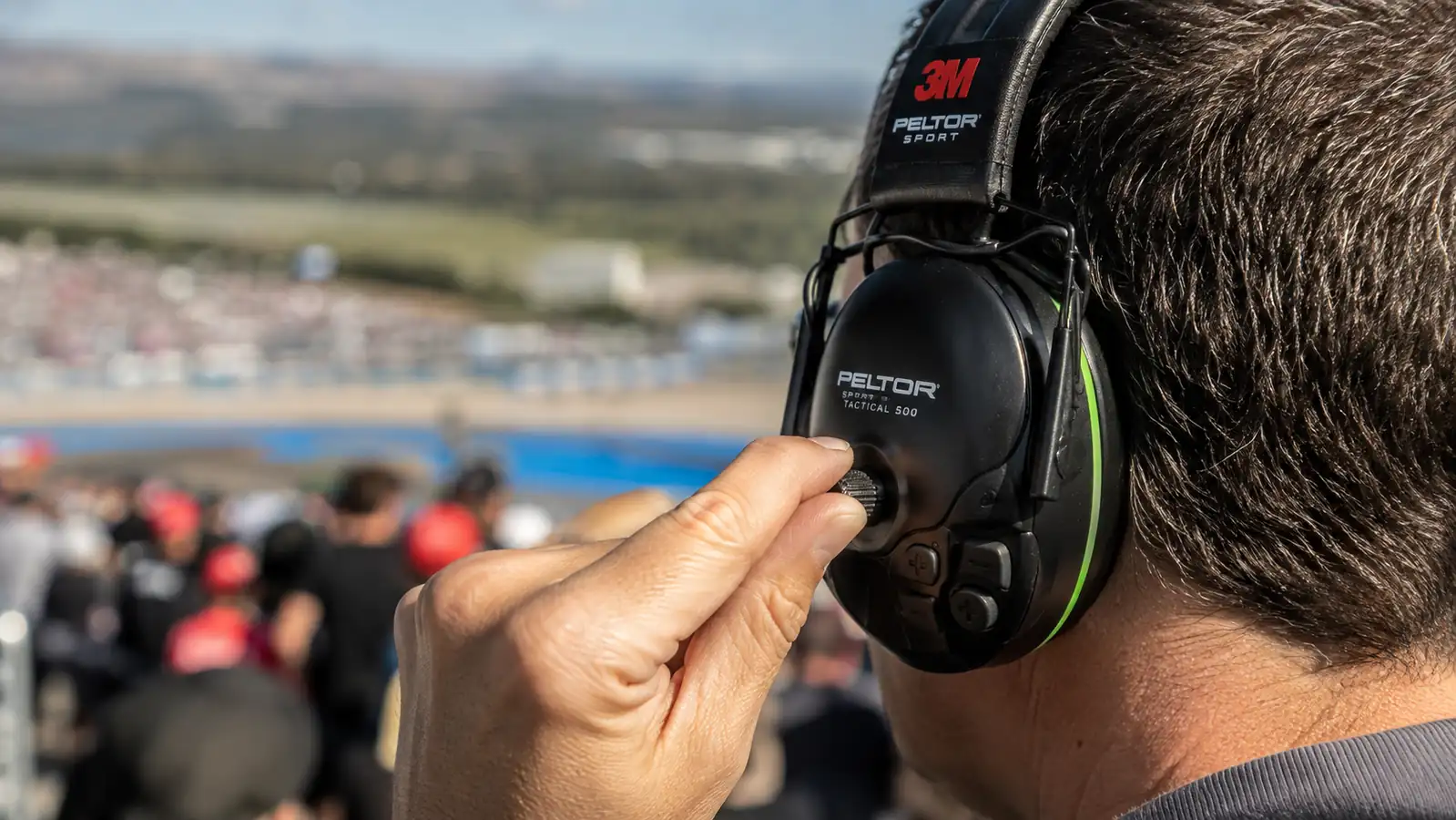 Hand adjusting the volume dial on a pair of black Peltor Sport Tactical 500 electronic earmuffs