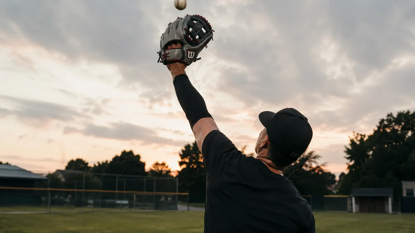 Outfielder extending a tan leather glove to catch a fly ball at a sports complex
